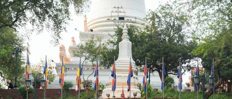 Una gran estupa blanca con una estatua dorada al frente, rodeada de banderas y un pequeño santuario.
