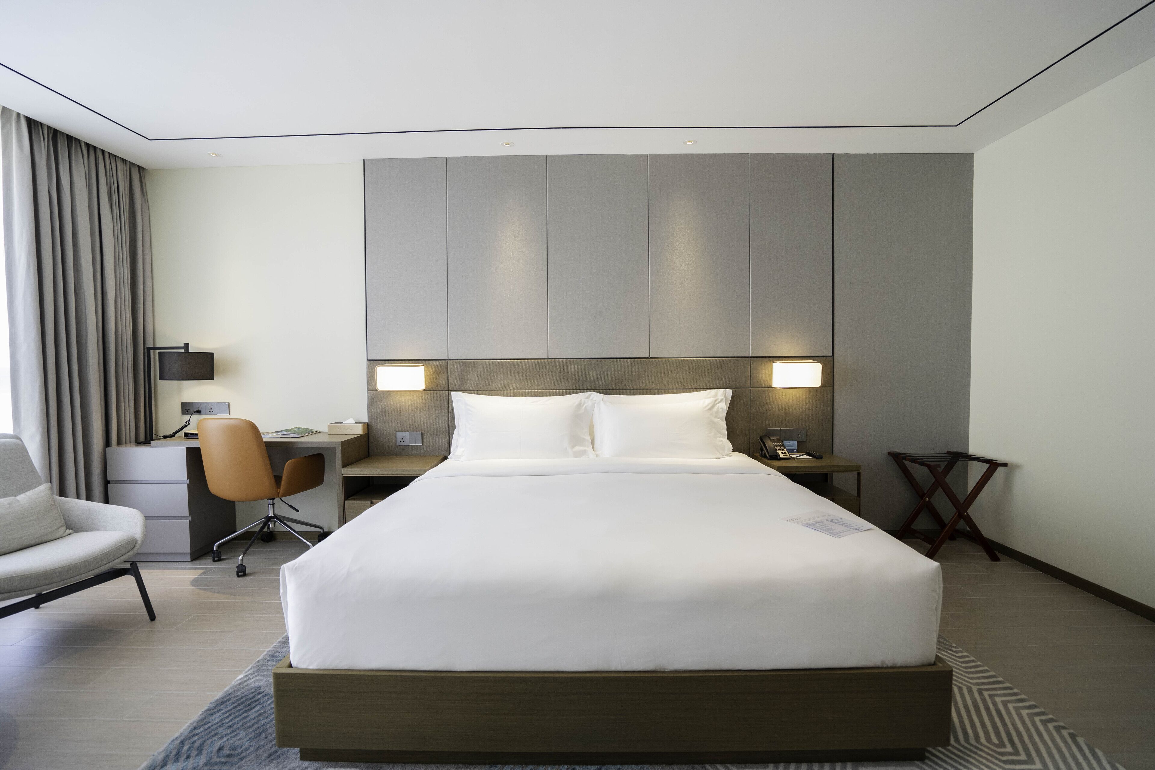 A modern hotel room with a large bed, a desk, a chair, and a small table.