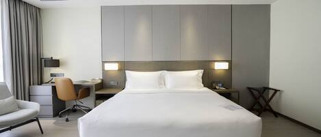 A modern hotel room with a large bed, a desk, a chair, and a small table.
