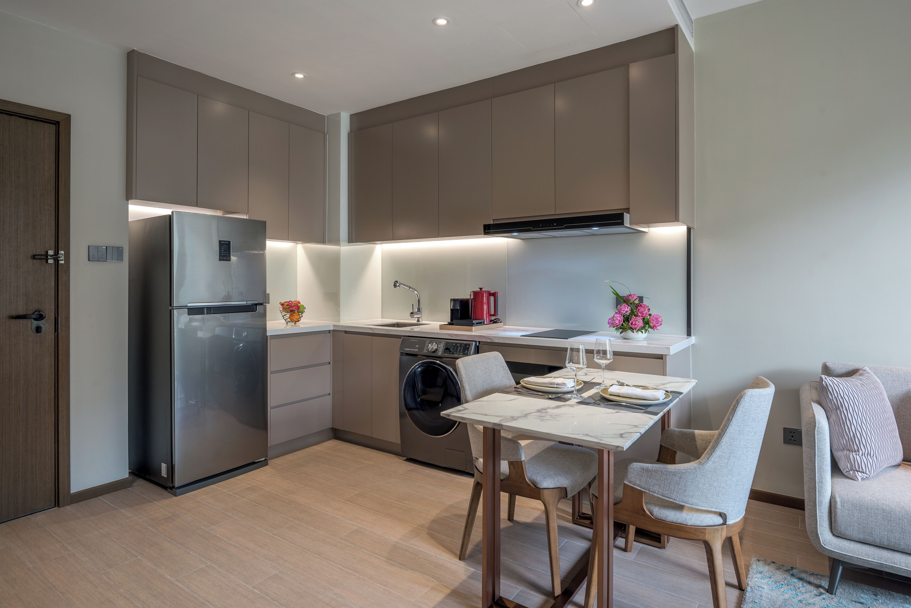 A modern kitchen with a built-in dishwasher, a stainless steel refrigerator, and a dining area with a table and chairs.