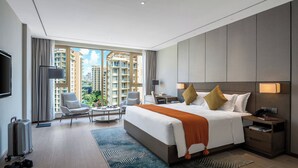 Een moderne hotelkamer met een groot bed, een bureau, een stoel en uitzicht op hoogbouw.