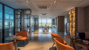 Een modern interieur met oranje stoelen, een glazen tafel en uitzicht door grote ramen.
