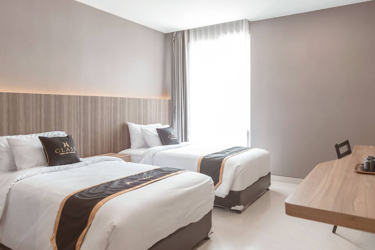 A hotel room with two beds, a wooden dining table, and a large window with curtains.