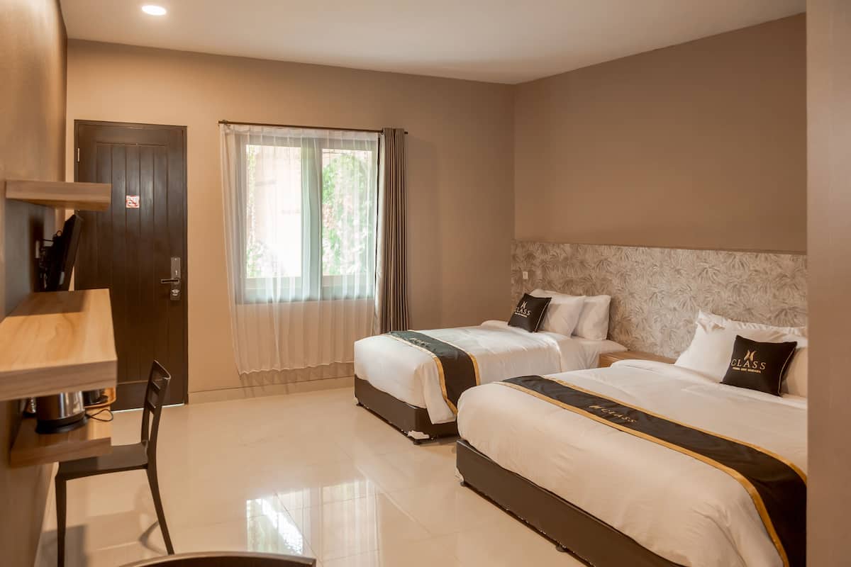 A hotel room with two beds, a desk, and a window with curtains.