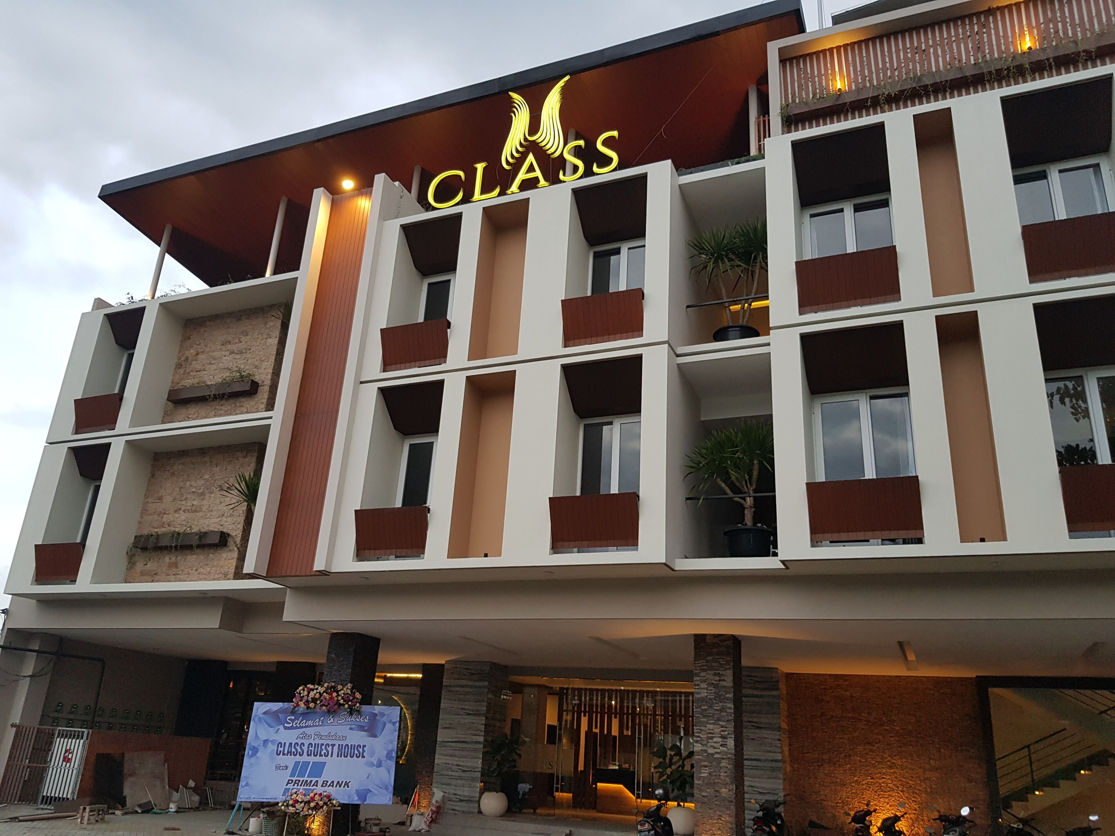 Ein mehrstöckiges Hotel mit Balkonen, einem Schild mit der Aufschrift „CLASS“ und einer Werbetafel für ein Gästehaus.