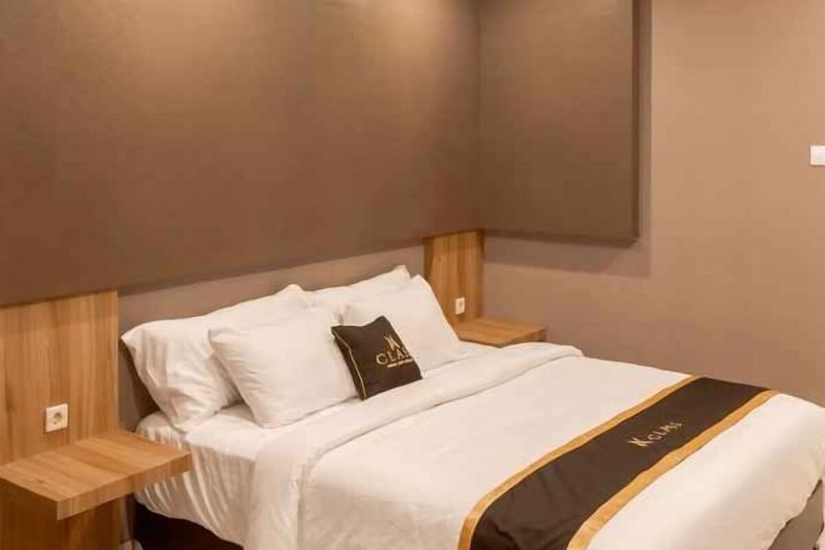 A hotel room with a bed, a nightstand, and a wall-mounted light fixture.