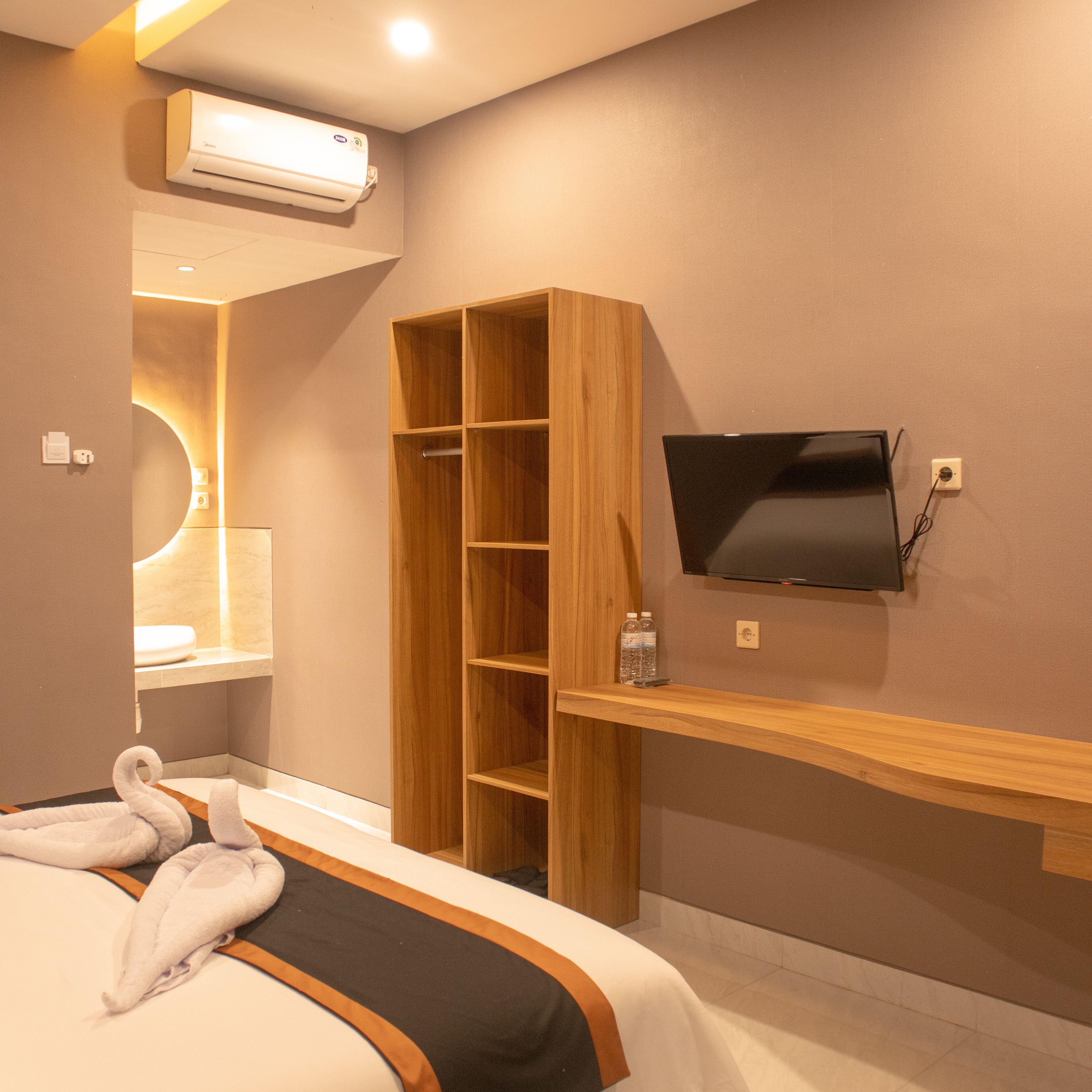 Ein Hotelzimmer mit einem Bett, einem an der Wand montierten Fernseher, einem Holzschrank und einer Klimaanlage.