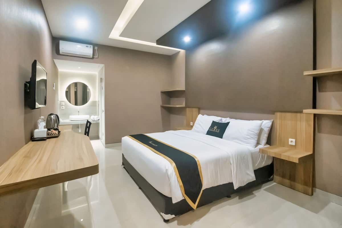 A modern hotel room with a large bed, a wooden desk, a mirror, and a built-in vanity with a round mirror.
