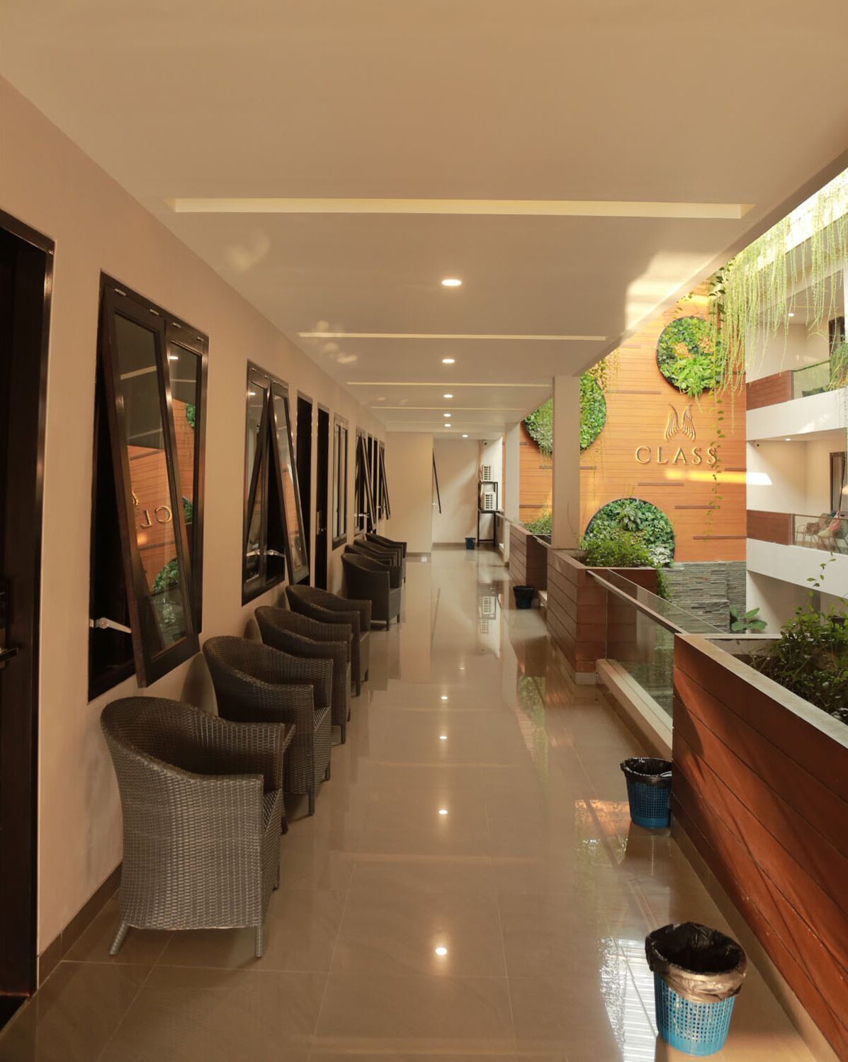 A hotel corridor with wicker chairs, a reception area with a wooden counter and greenery, and a clear view of the reception desk.