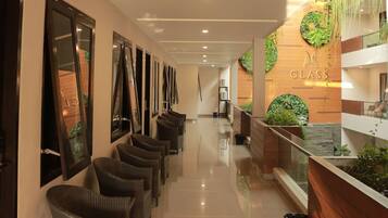A hotel corridor with wicker chairs, a reception area with a wooden counter and greenery, and a clear view of the reception desk.