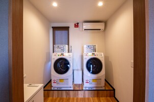 A laundry room with two stacked front-loading washing machines, a small window, and an air conditioning unit on the wall.