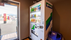 A vending machine with various products, a trash bin, and a door leading outside. - HOTEL R9 The Yard Isa (Isa)