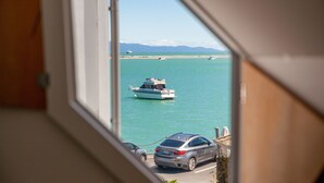 Une vue depuis une fenêtre donnant sur une marina, avec des bateaux et une voiture garée au bord de l’eau.