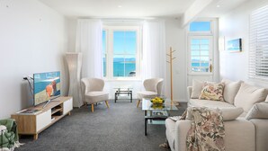 Un salon moderne doté d’une grande fenêtre, d’un téléviseur à écran plat, d’un canapé, de deux fauteuils, d’une table basse et d’une petite table d’appoint.