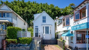 Une maison blanche à deux étages, dotée d’un porche à l’avant et d’un petit jardin.