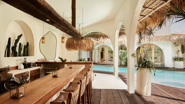 A bar area with wooden furniture, a pool, and tropical plants. - Stunning 4BR Villa With Rice Field View in Umalas (Kerobokan)