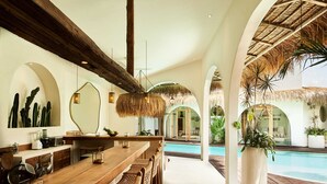 A modern kitchen with a long wooden bar, a large mirror, and a view of a pool. - Stunning 4BR Villa With Rice Field View in Umalas (Kerobokan)