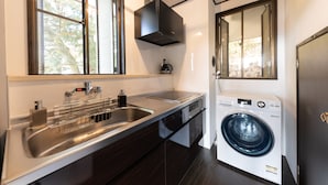 Una cocina moderna con un lavamanos de acero inoxidable, lavadora integrada y una ventana con persianas.