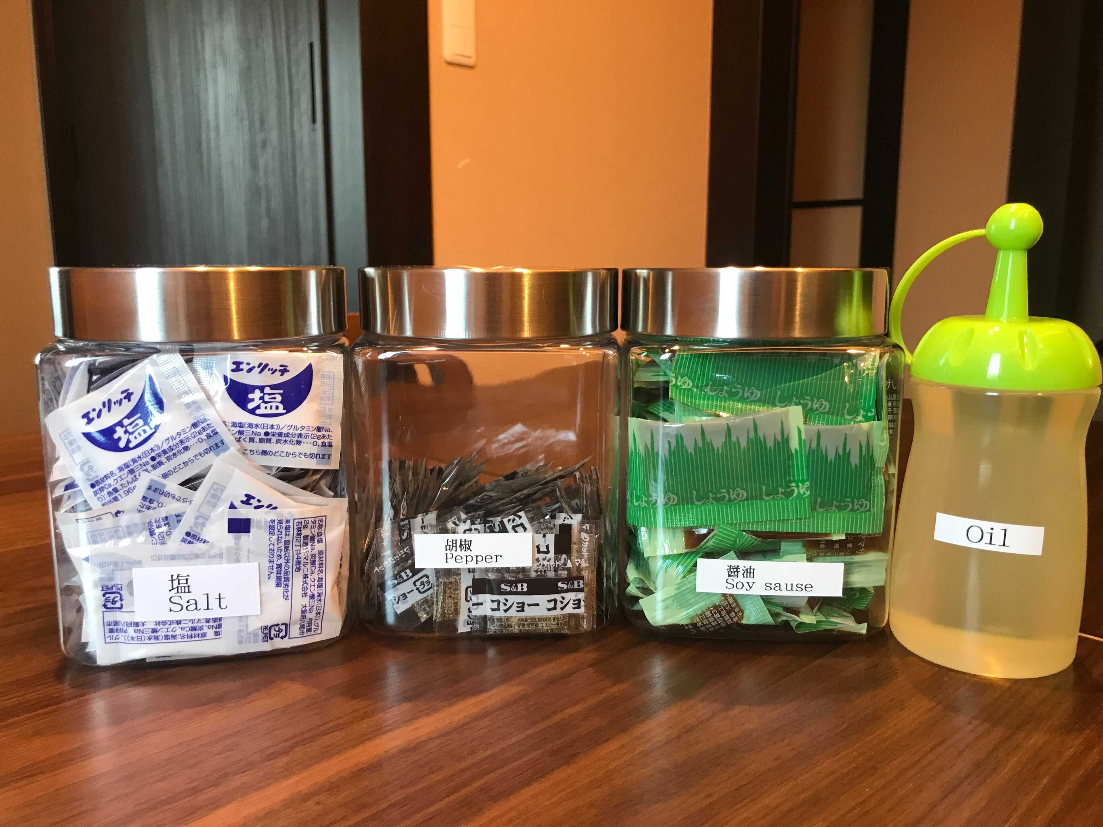 Quatre récipients sur une surface en bois : l’un contient des sachets de sel, l’autre du poivre, le troisième de la sauce soja et le quatrième de l’huile.