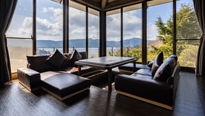 Una habitación moderna con un ventanal grande, un sofá, una mesa y vistas a montañas y una masa de agua.