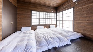 Una habitación con paredes y techo de madera, dos camas con ropa blanca y ventanas grandes con diseños de cuadrícula.