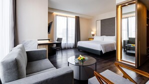 A hotel room with a bed, a sofa, a desk, a round coffee table with fruit, and a large mirror. - Quest Prime Pemuda - Semarang (Semarang)