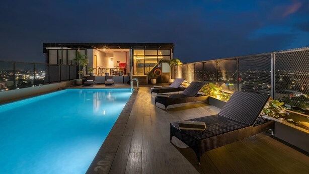 A rooftop pool area with lounge chairs, a modern building with glass doors, and a city view at dusk. - Quest Prime Pemuda - Semarang (Semarang)