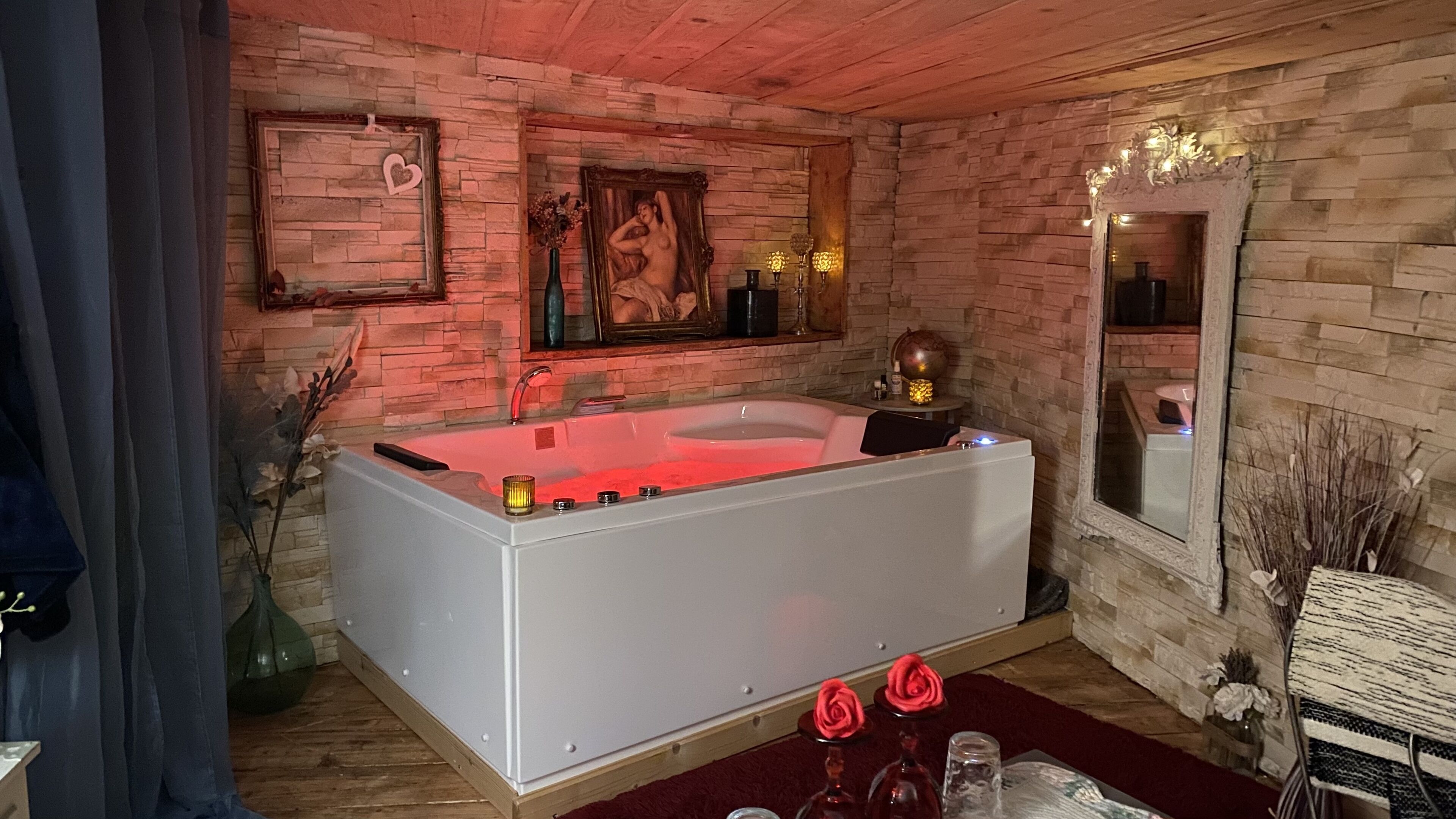 A modern bathroom with a freestanding bathtub, a large mirror, and a stone wall backdrop.