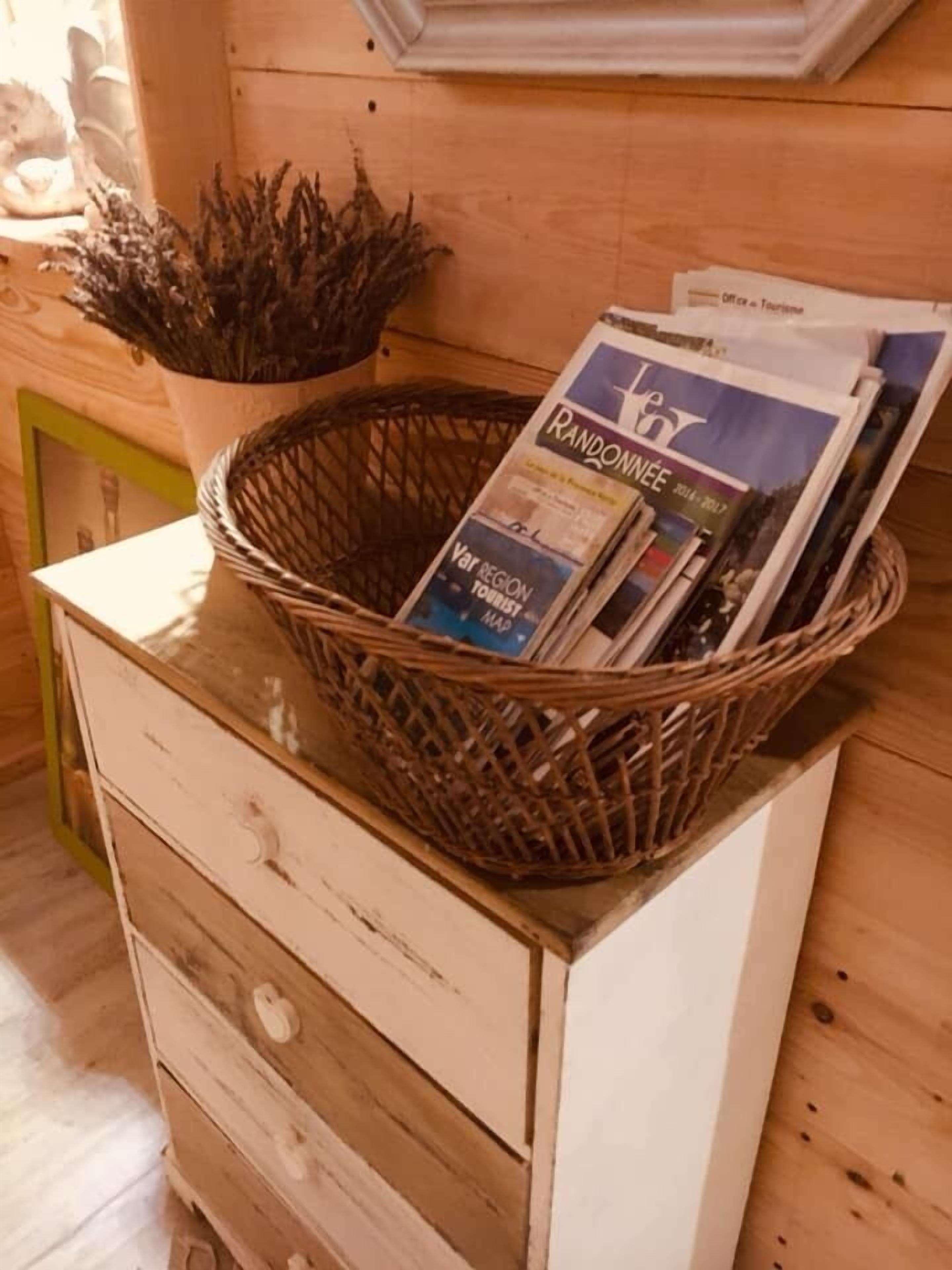 A wicker basket filled with magazines on a wooden dresser.