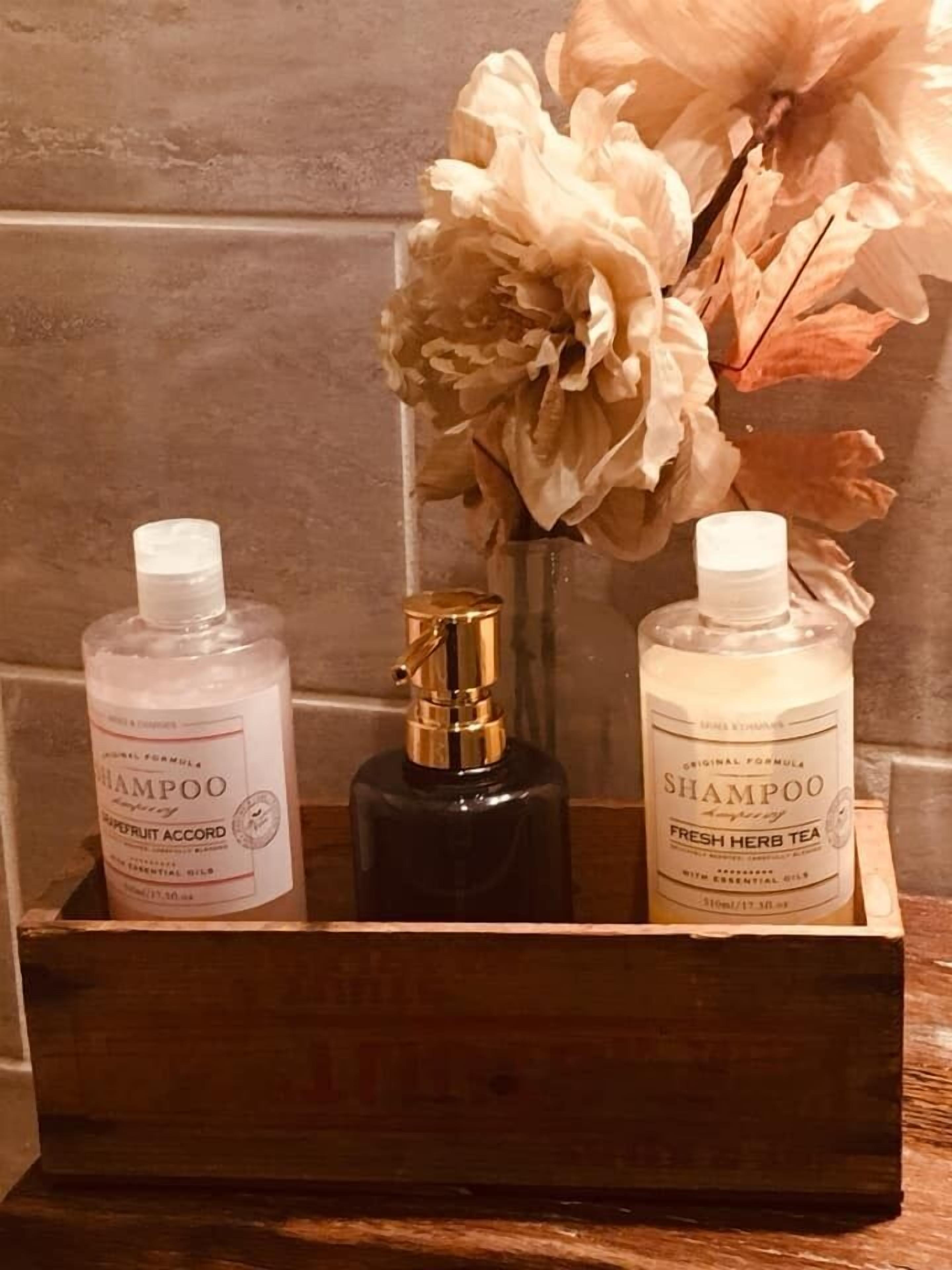 Une boîte en bois contenant trois bouteilles de shampoing, dont l’une est étiquetée « Thé aux herbes fraîches ».