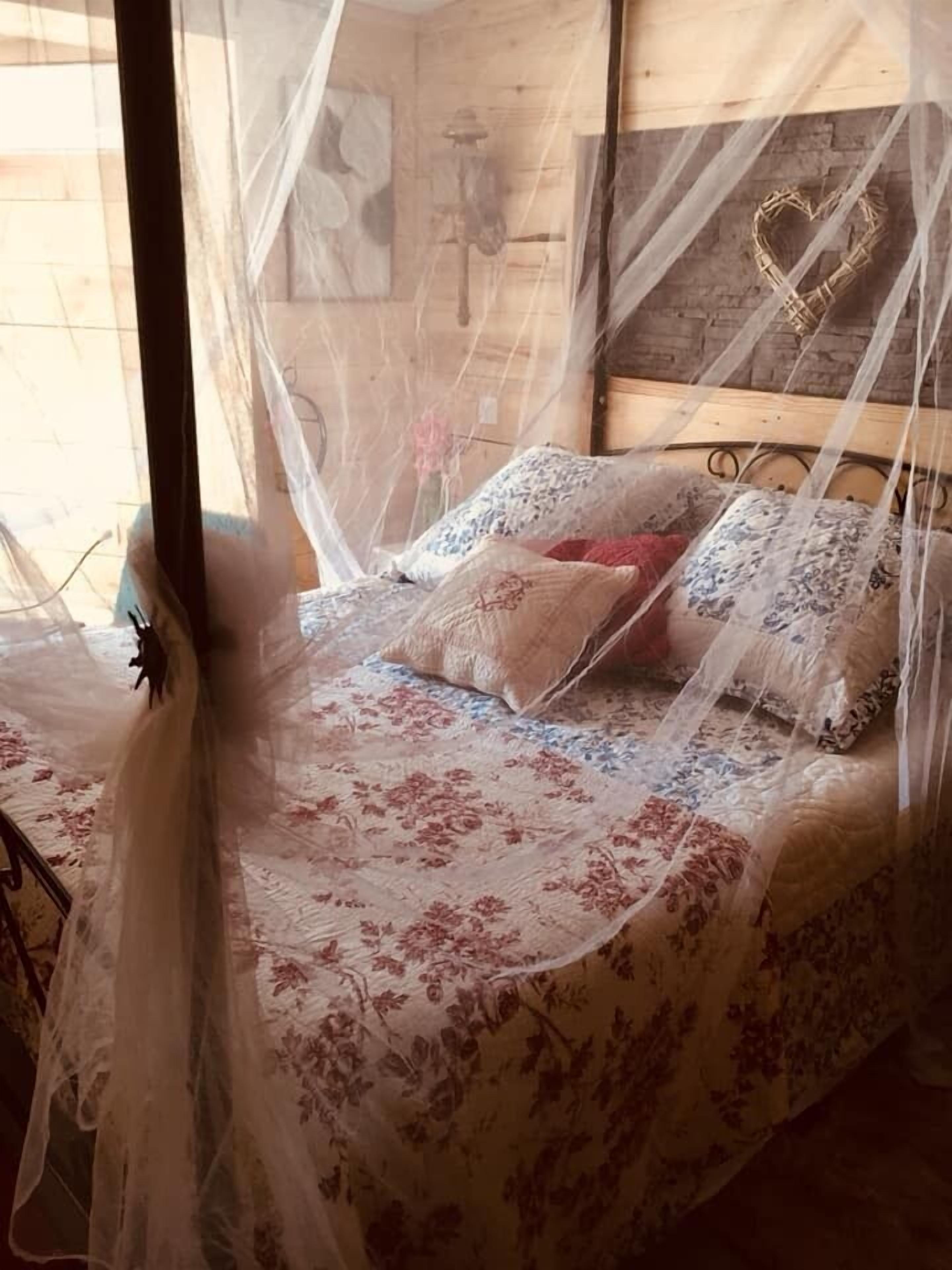 Una cama con una colcha estampada con motivos florales, una decoración en forma de corazón en la cabecera y una mosquitera.