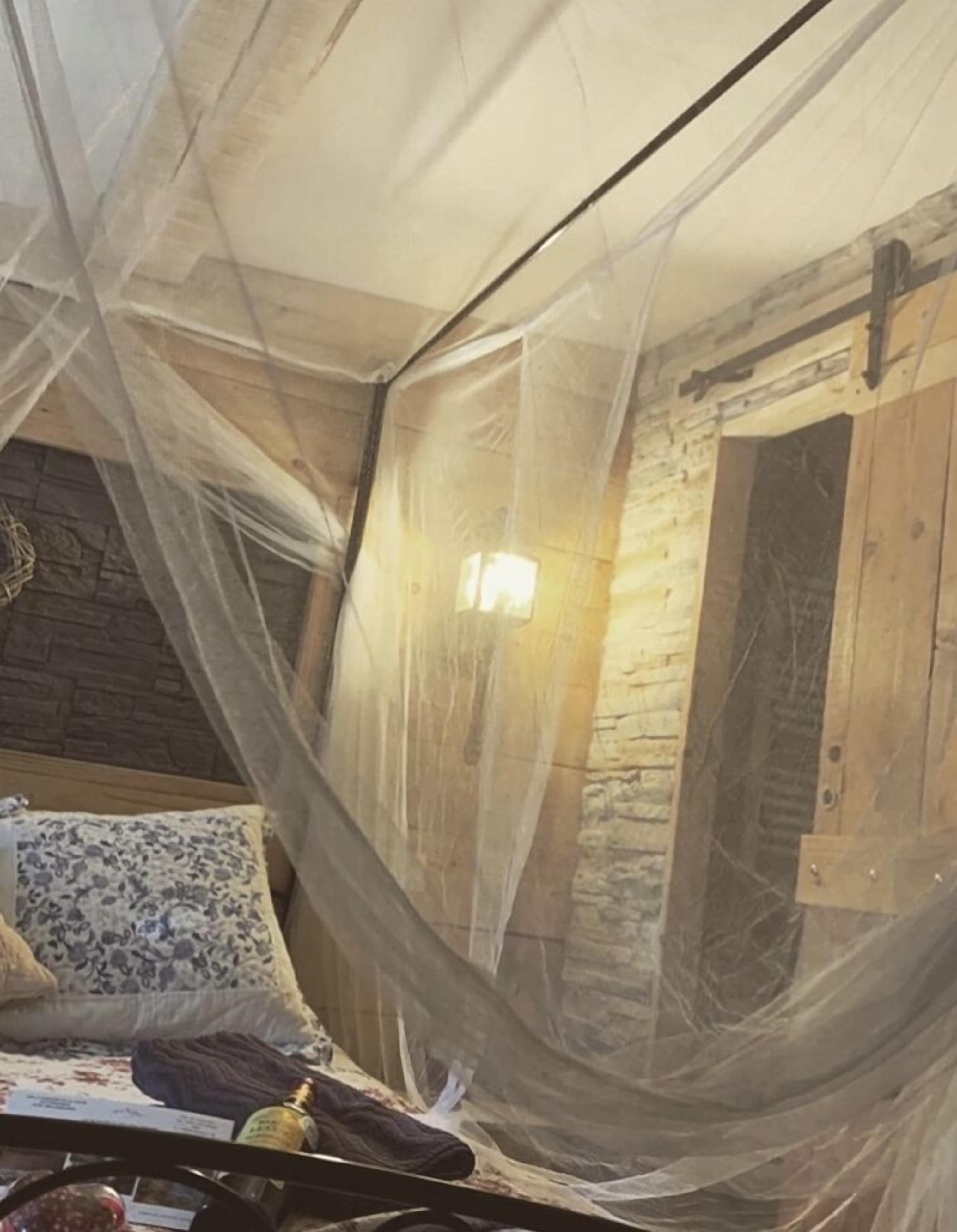 Una habitación con una cama cubierta por una mosquitera, paredes de madera y un detalle en pared de piedra.