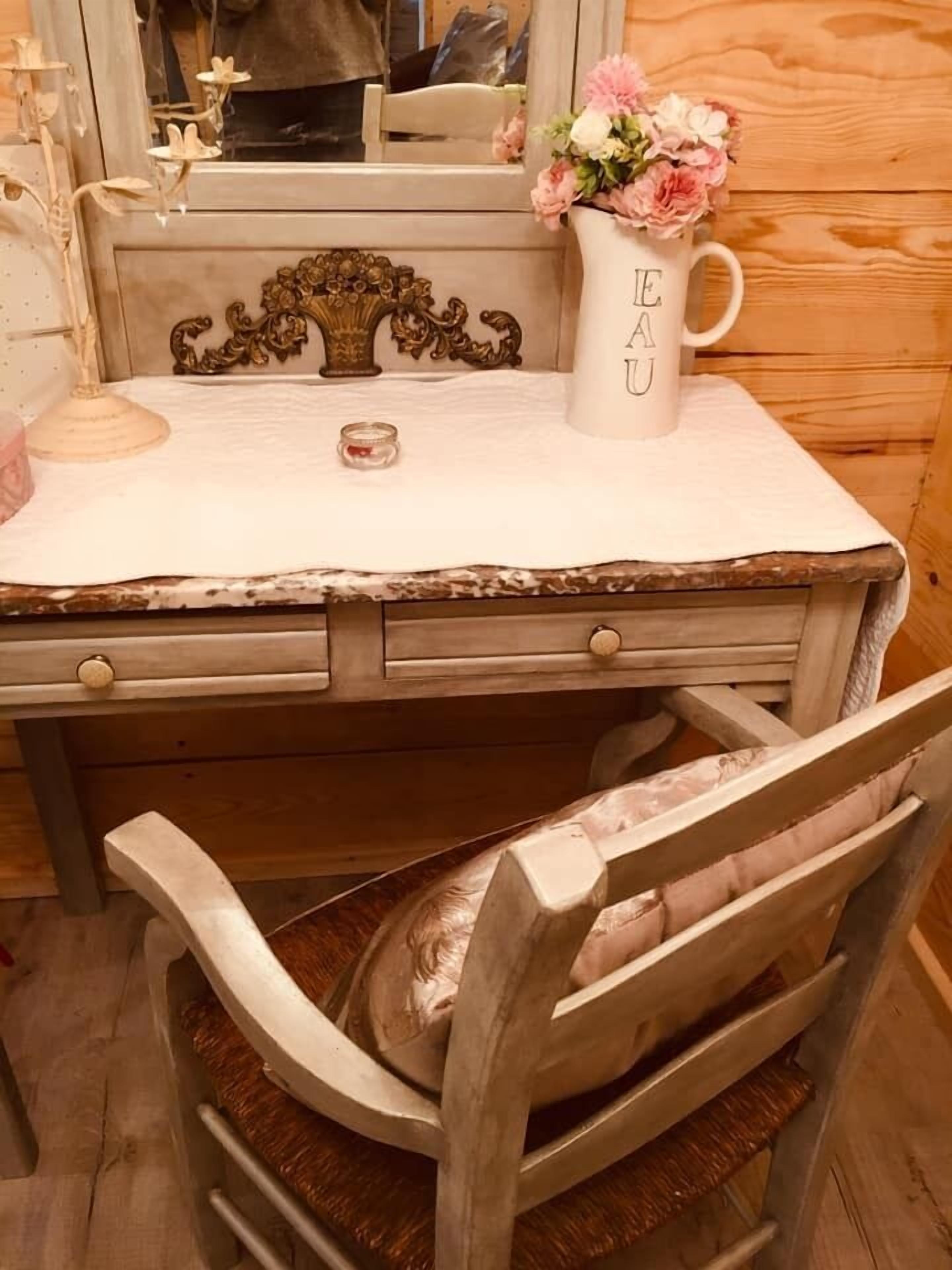 A wooden desk with a white marble top, a vintage-style chair, and a vase with flowers.