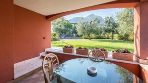 Une table en verre entourée de chaises, une vue sur un jardin avec des arbres et une montagne, et un bâtiment en arrière-plan.