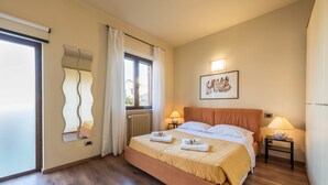 Une chambre à coucher comprenant un lit, deux tables de chevet, une fenêtre avec des rideaux, un radiateur, un miroir fixé au mur et un tableau encadré.