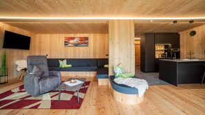 Ein modernes Interieur mit Holzboden, einem Flachbildfernseher, einer Couch, einem Sessel, einem kleinen Tisch und einer Küchenzeile.