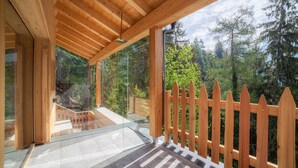 Eine Holzterrasse mit Glasgeländer, die auf einen bewaldeten Bereich blickt.