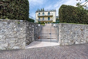 Un muro de piedra con una verja que da a un edificio con balcón y escalera.