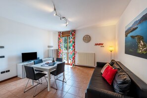 Una sala de estar moderna con comedor, un sofá de cuero negro, un televisor y un cuadro en la pared.