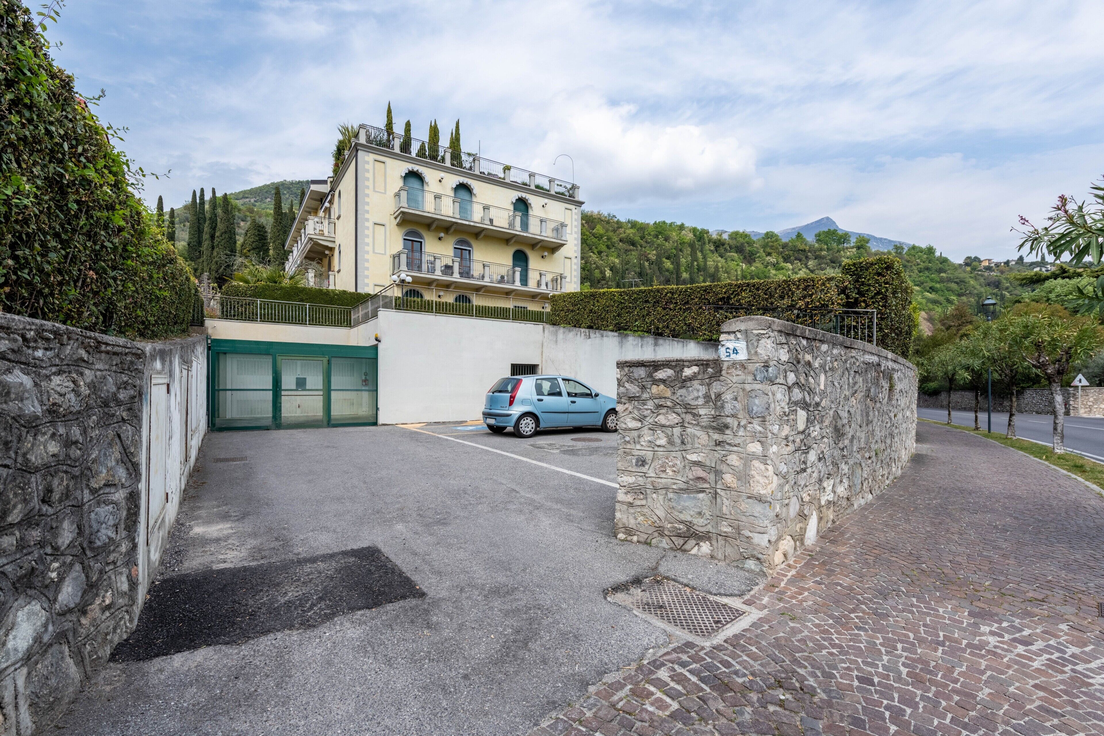Ein Gebäude mit einer Steinmauer, einem blauen Auto und einem Berg im Hintergrund.