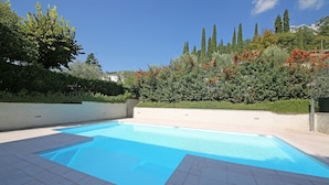 Una piscina con borde de baldosas, rodeada de vegetación y árboles altos.