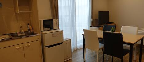 A compact kitchen with a microwave, refrigerator, and sink. There is a dining area with a table and chairs.