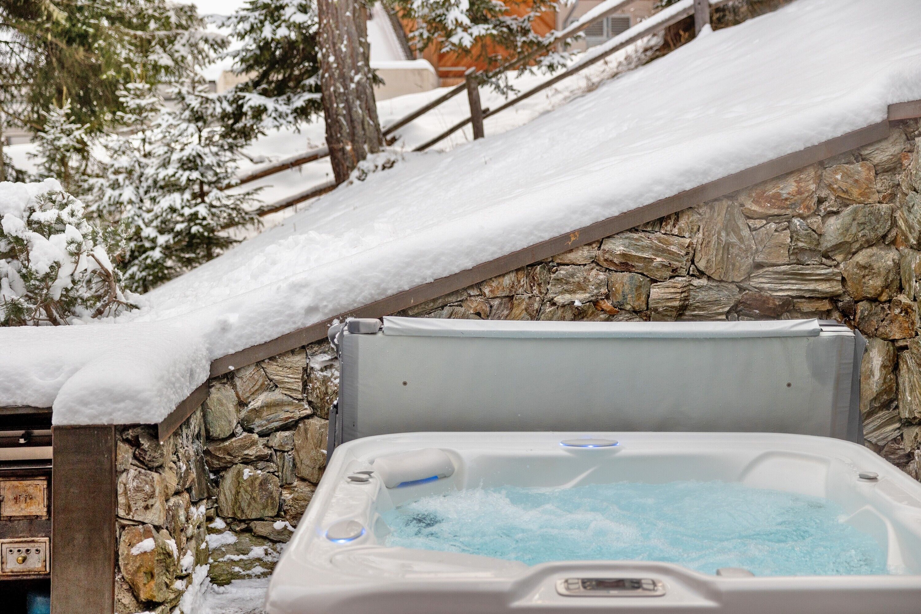 Un muro de piedra con un jacuzzi, parcialmente cubierto de nieve.