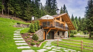 A wooden chalet with a stone pathway leading to the entrance, surrounded by lush greenery and trees. - High Luxury Chalet "K Lodge Mountain" with Mountain View, Whirlpool and Sauna (Olang)
