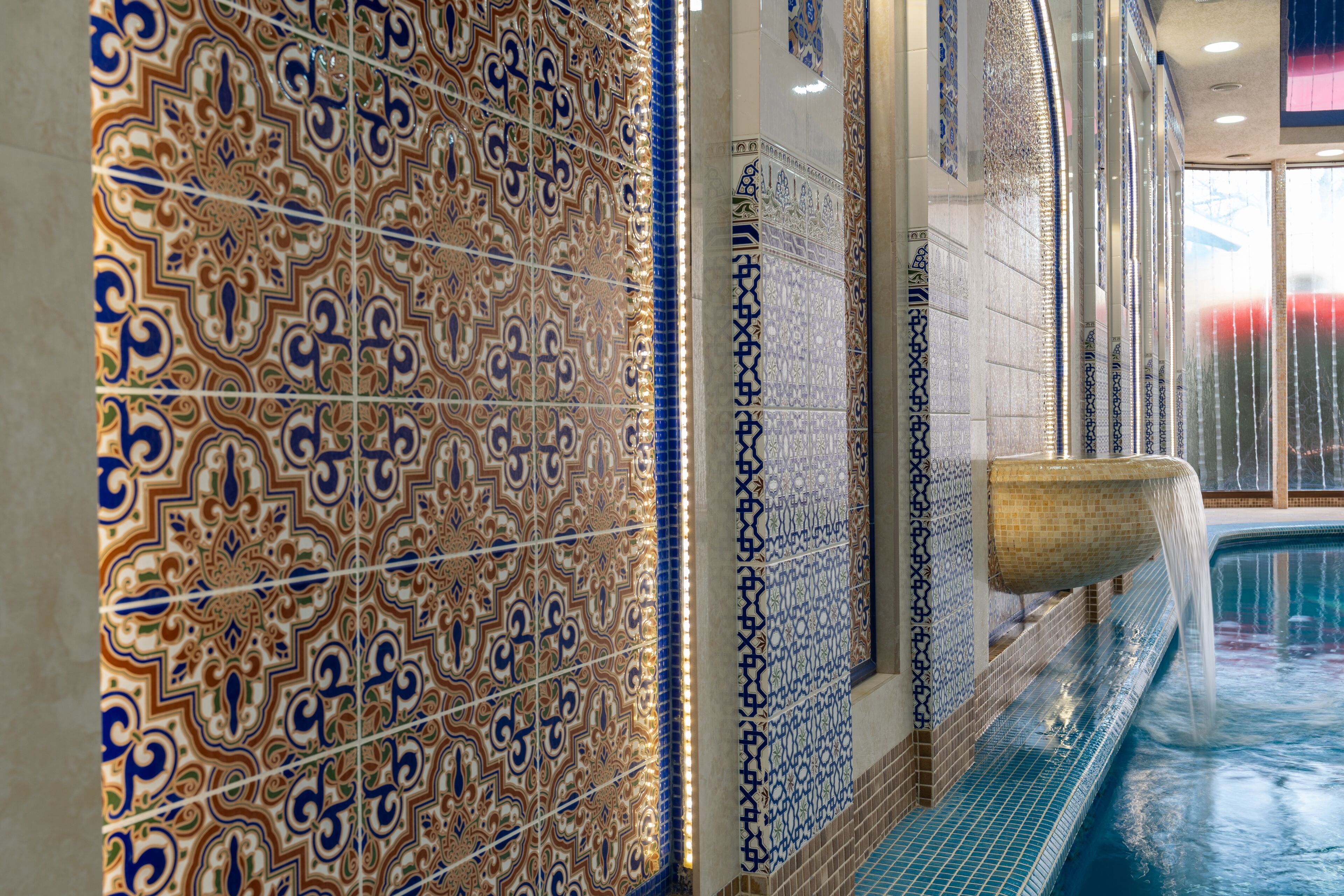 Une piscine ornée de motifs complexes en mosaïque et agrémentée d’un élément décoratif aquatique.