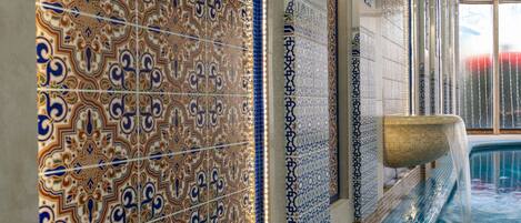 Une piscine ornée de motifs complexes en mosaïque et agrémentée d’un élément décoratif aquatique.