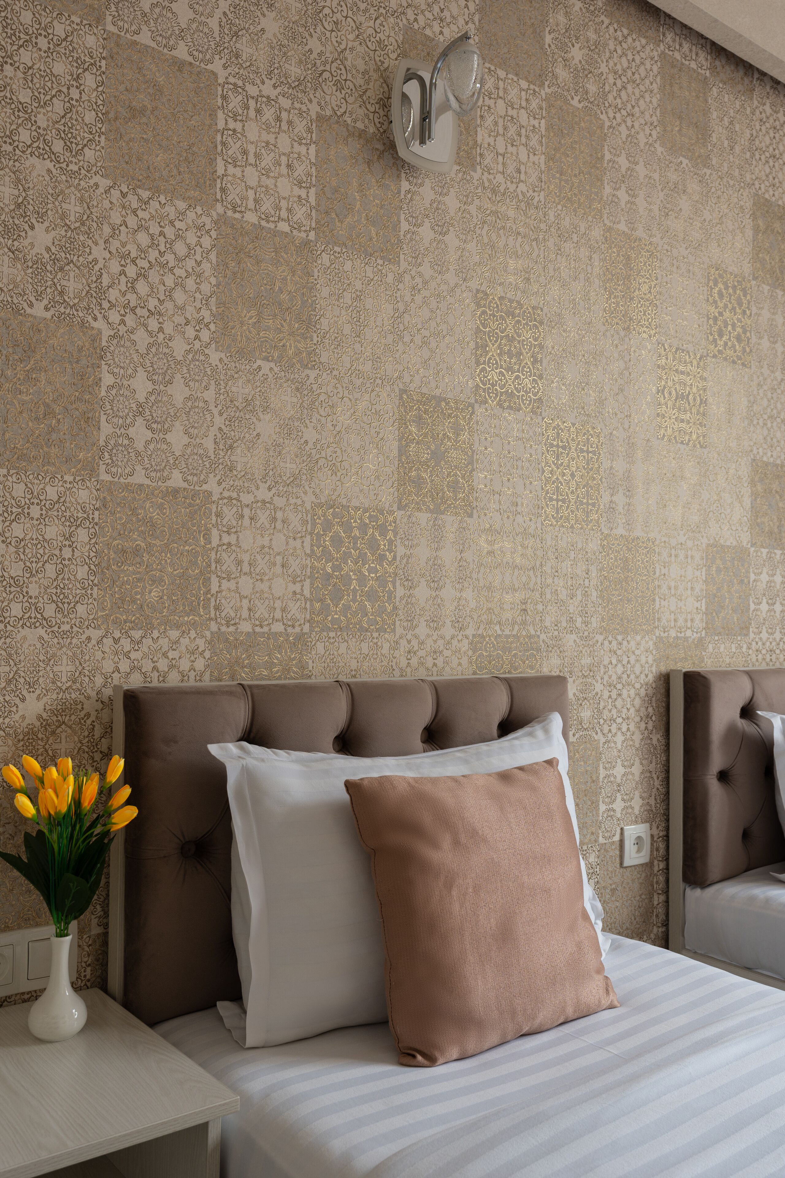 Ein Hotelzimmer mit Wandverkleidung, einem Bett mit Kopfteil, einem Nachttisch mit Blumenvase und einem Spiegel.