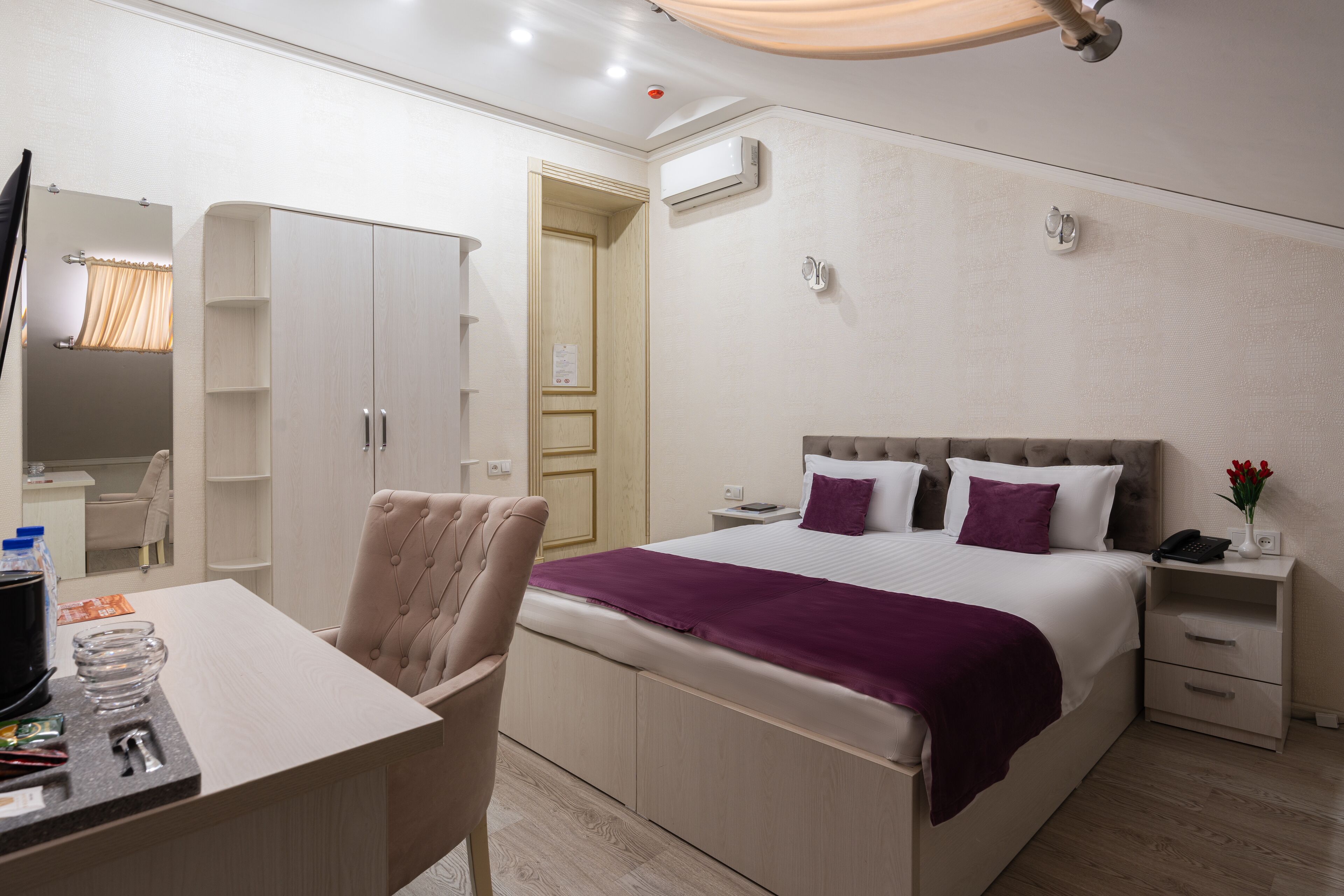 A hotel room with a bed, bedside tables, a desk, a chair, and a wardrobe.
