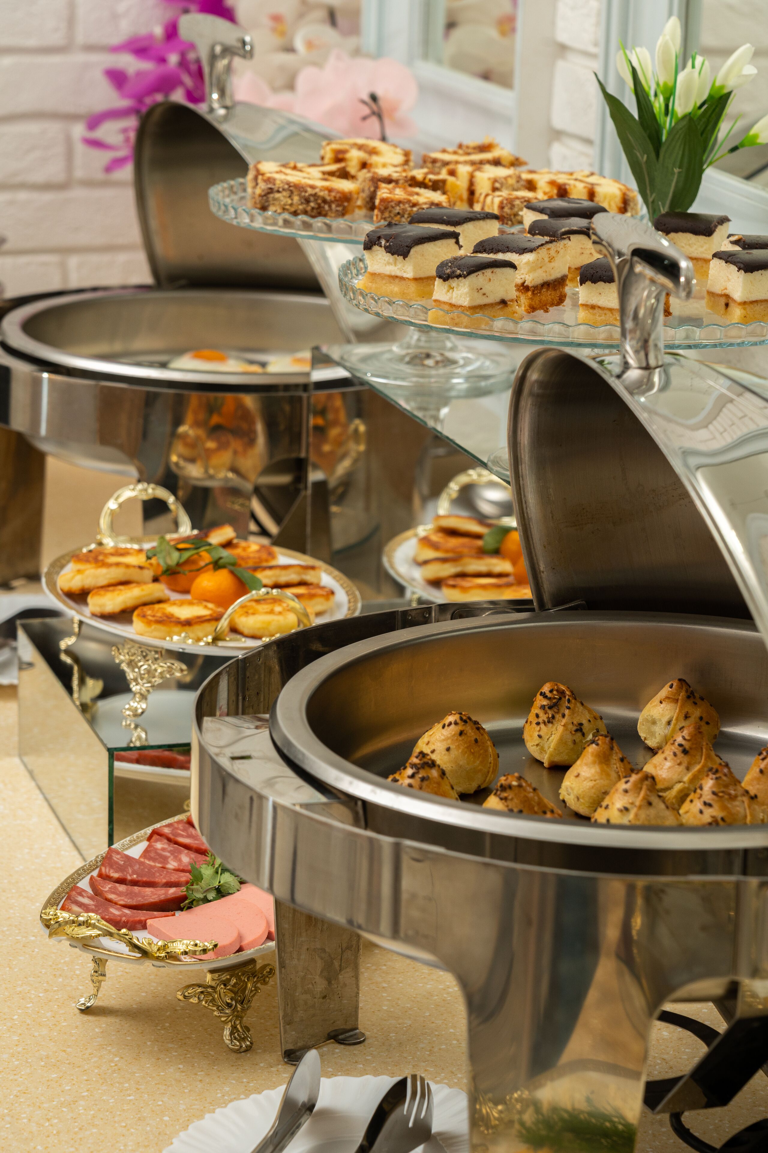 A buffet with various food items, including pastries, sandwiches, and a dish with meat.