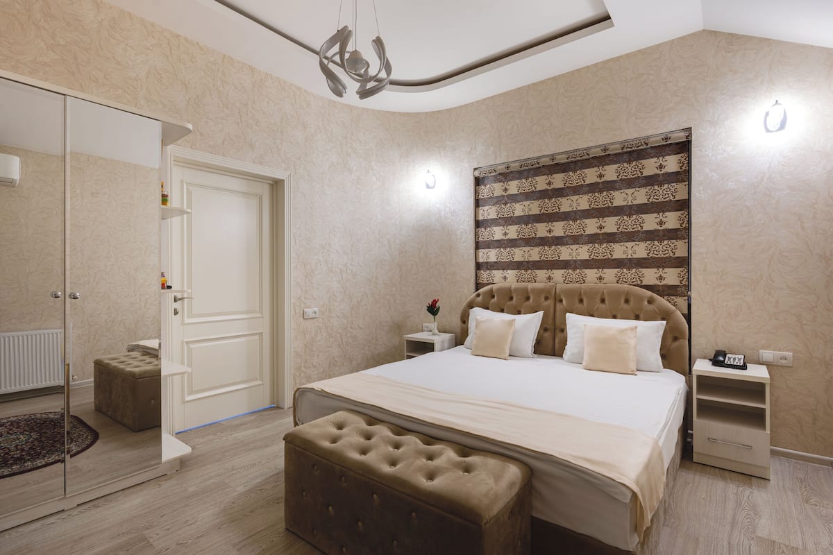 A bedroom with a large bed, a headboard with a patterned design, a nightstand, and a small table with a lamp.